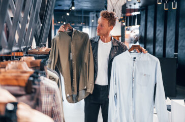 Big choice. Young guy in modern store with new clothes. Elegant expensive wear for men